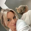 Eine junge Frau mit blondem Haar, die lächelnd in die Kamera schaut, während ihr Spiegelbild eine beigefarbene Haarklammer zeigt.