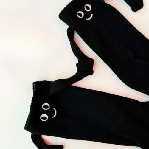 Ein Paar schwarze Socken mit lachendem Gesicht und angenähten Armen, die sich an den Händen halten.