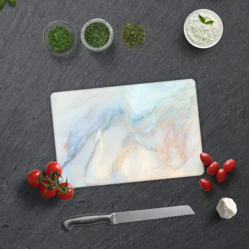 Glas Schneidebrett in Marmoroptik auf einer dunklen Arbeitsfläche, umgeben von frischen Tomaten, Kräutern, Knoblauch, einem Messer und einem Küchentuch.
